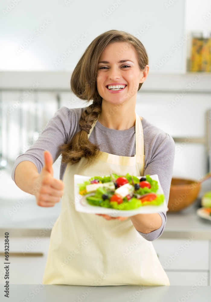 Happy young housewife showing greek salad and thumbs up Happy young housewife showing greek salad and thumbs up
