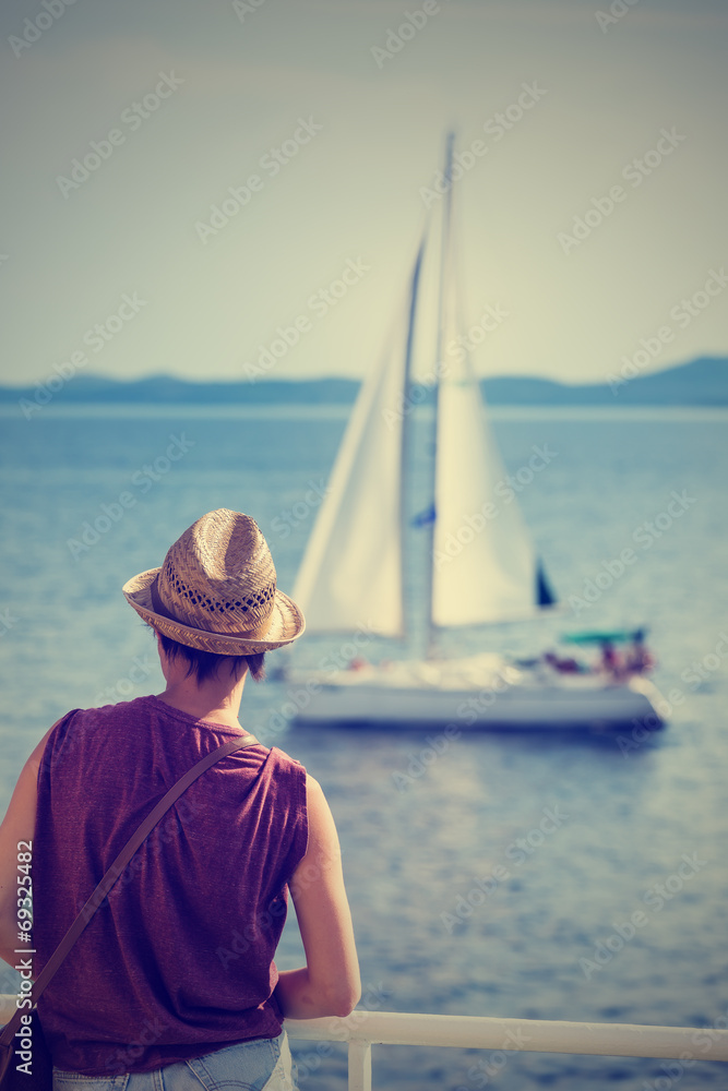 Fototapeta premium Female passenger on the deck of the ferry watching the sailboat