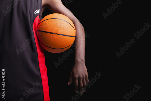 Basketball player standing with a basket ball on black backgroun