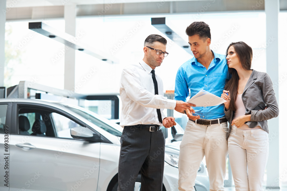 Young Couple Signing a Contract in Car Showroom. Young Couple Signing a Contract in Car Showroom.
