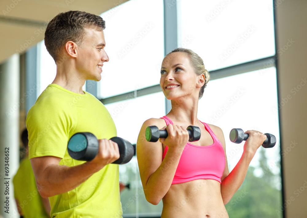 smiling man and woman with dumbbells in gym