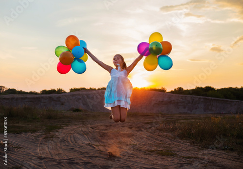 Happy girl with colorful balloons at sunset
