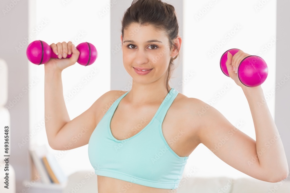 Fit brunette holding dumbbells smiling at camera Fit brunette holding dumbbells smiling at camera