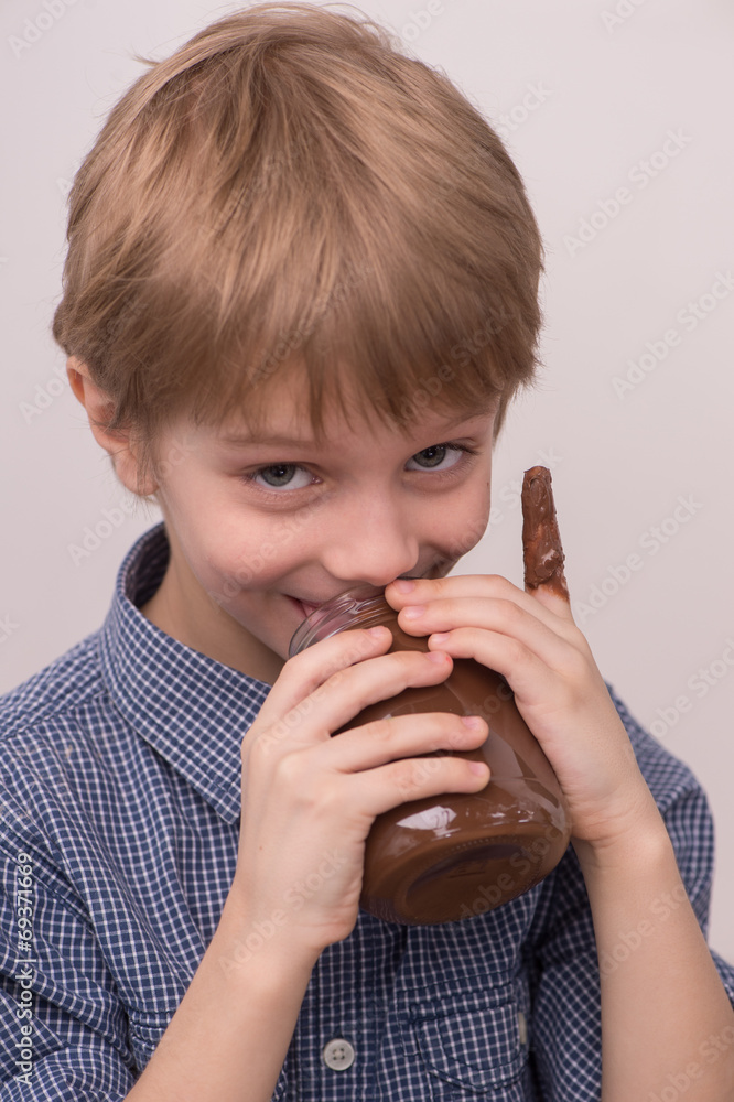 Child licks chocolate glaze from jar. Child licks chocolate glaze from jar.
