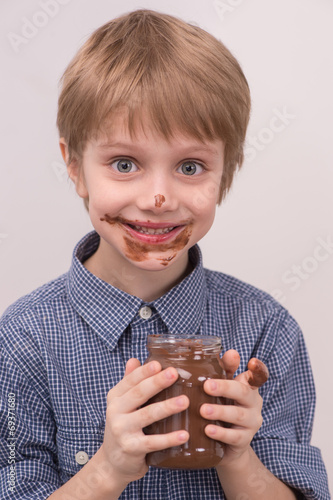 Smiling kid eating chocolate from jar.