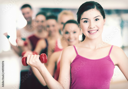 group of smiling people with dumbbells in the gym