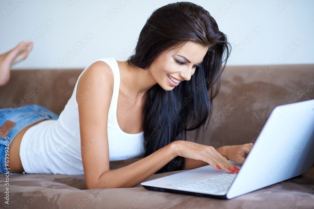 Young woman lying on a sofa using a laptop Young woman lying on a sofa using a laptop
