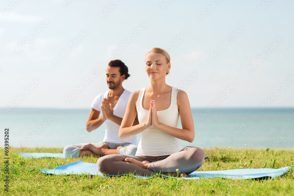 smiling couple making yoga exercises outdoors