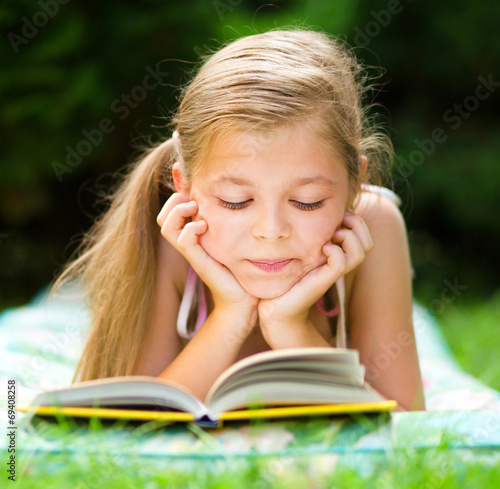 Little girl is reading a book outdoors