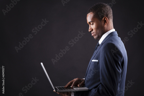 Young business man with a laptop over dark background