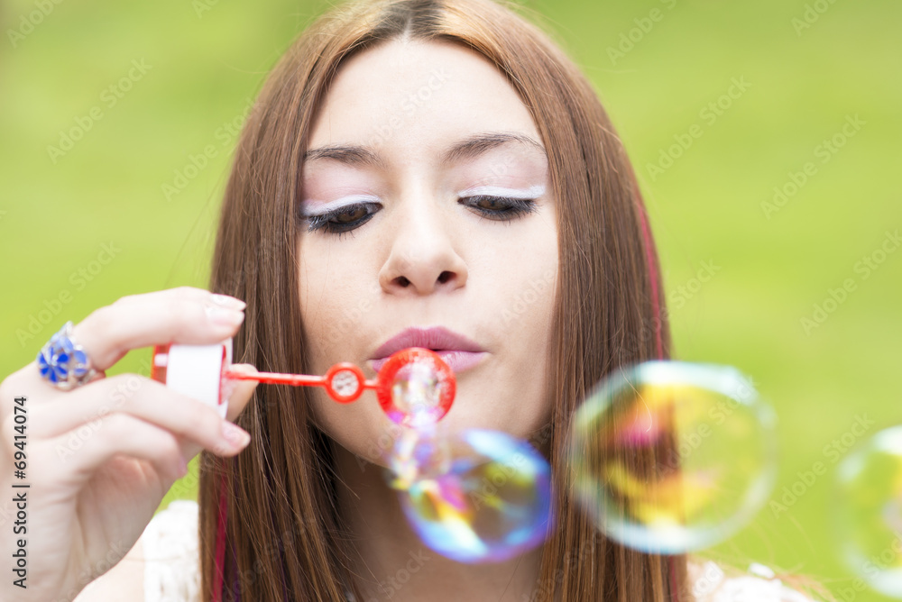 Closeup portrait of beautiful woman inflating colorful soap bubb