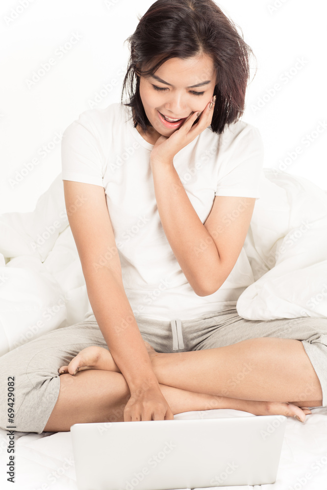 Smiling woman using a laptop while lying on her bed Smiling woman using a laptop while lying on her bed