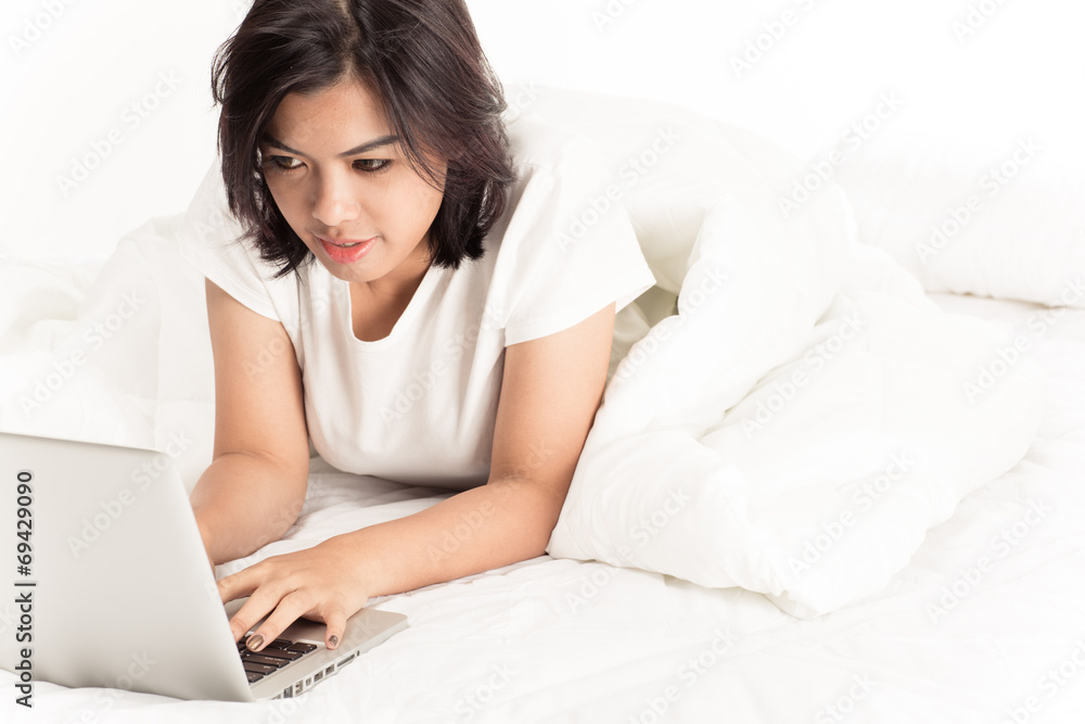 Smiling woman using a laptop while lying on her bed Smiling woman using a laptop while lying on her bed