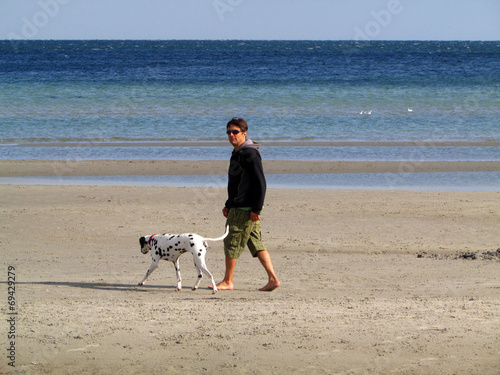 Mann spaziert mit Dalmatiner am Ostseestrand