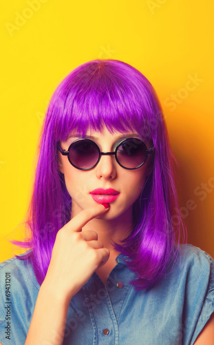 Beautiful girl with violet hair in sunglasses on yellow backgrou