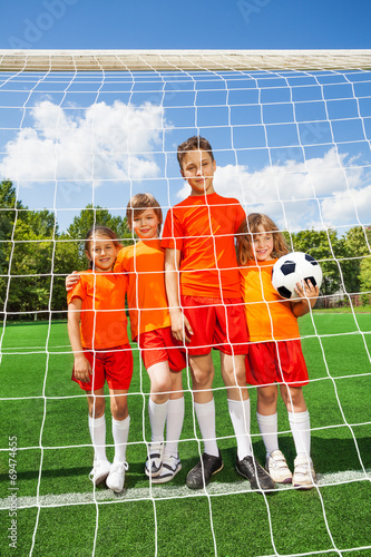 Kids stand in line with football behind woodwork