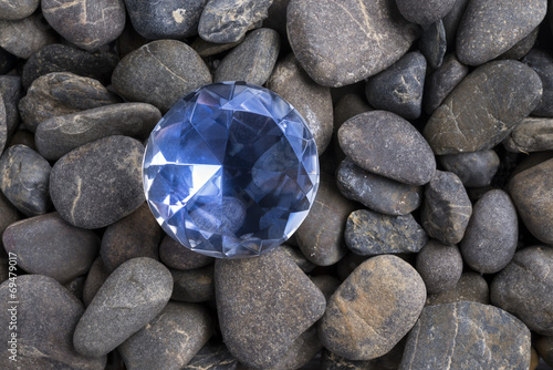 Obraz na płótnie Sparkling Blue Gemstone Resting on a Bed of Smooth River Stones