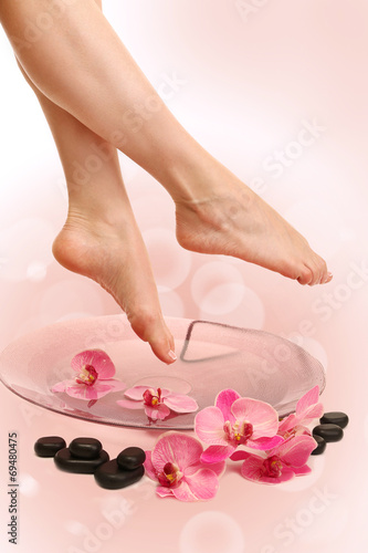 Female feet in spa bowl with water on bright background