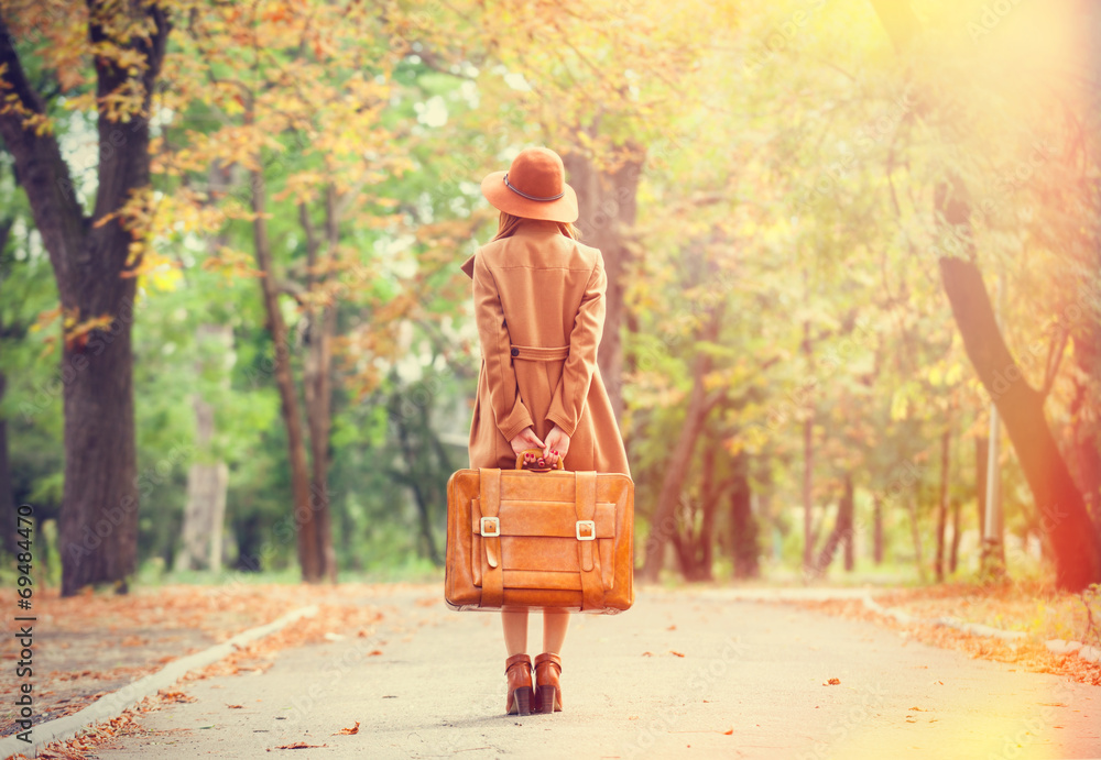 Obraz premium Redhead girl with suitcase in the autumn park.