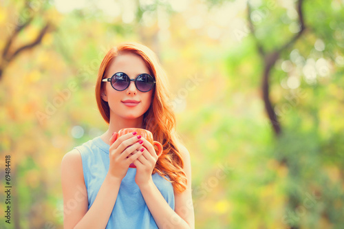 Successful redhead girl winh cup in the autumn park. photo