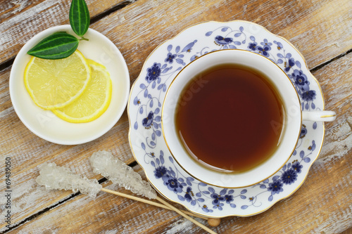 Black tea in vintage cup and lemon on wooden surface
