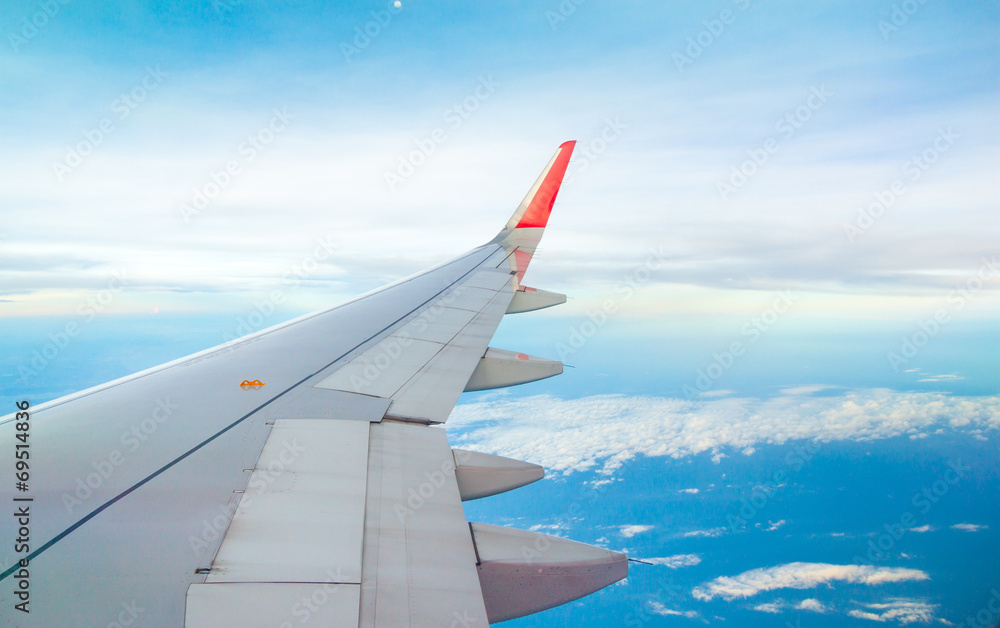Wing of airplane flying above the clouds in the sky Wing of airplane flying above the clouds in the sky