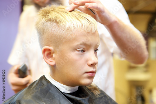Barber cutting hair of young boy by electric trimmer