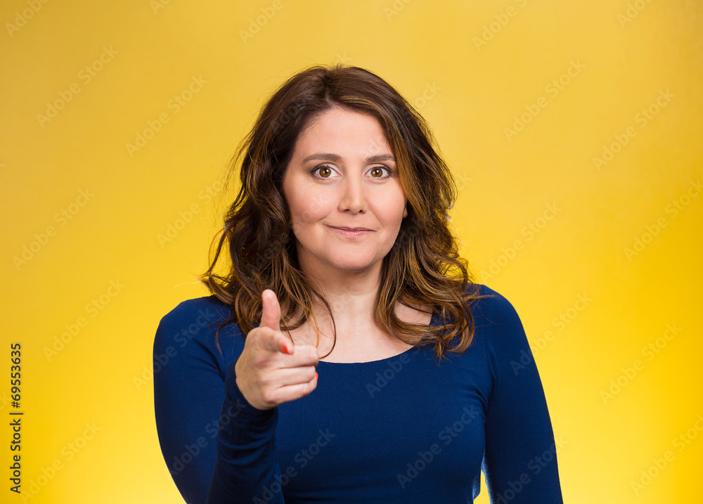 Woman smiling pointing finger towards you yellow background Woman smiling pointing finger towards you yellow background