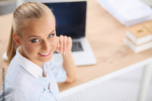 Attractive businesswoman sitting on a desk with laptop in the o