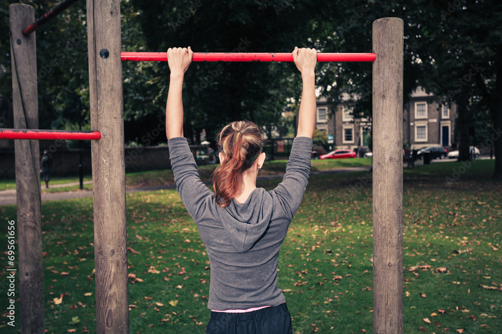 Fototapeta premium Young woman doing pullups in the park