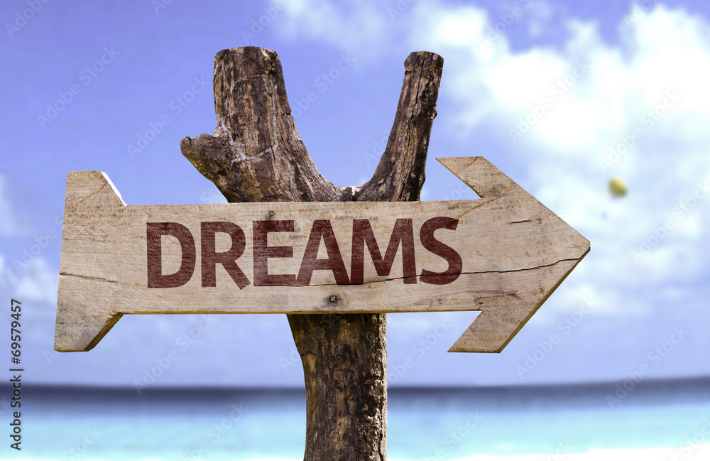 Dreams wooden sign with a beach on background