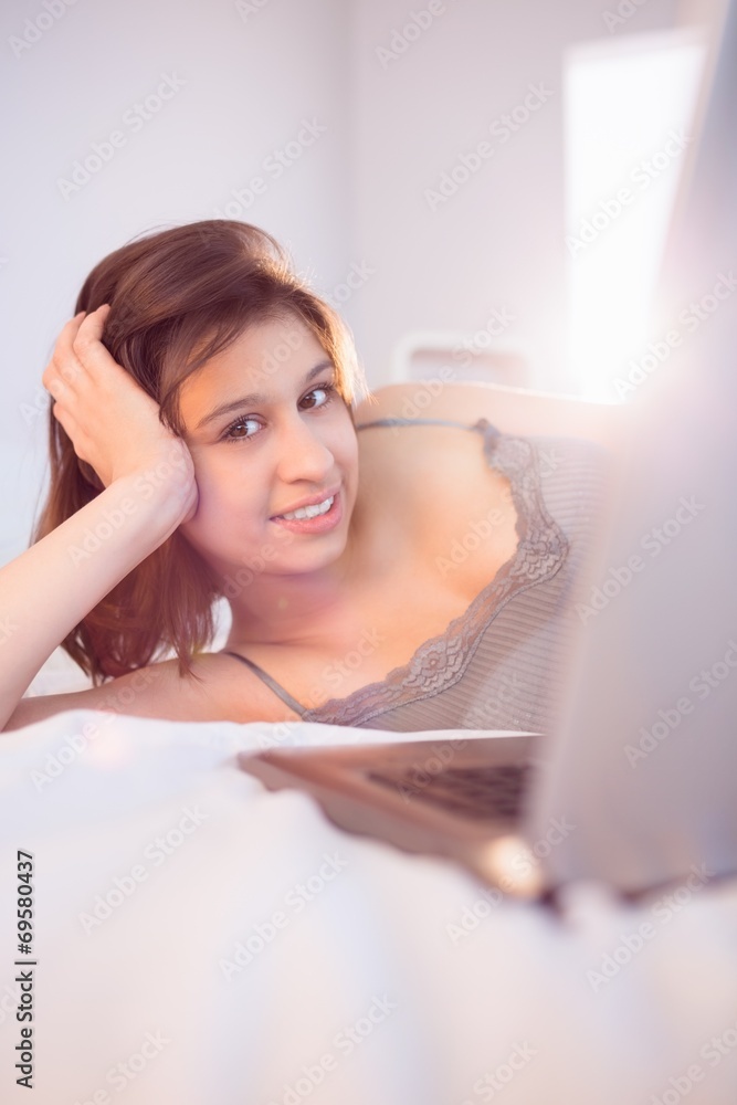 Beautiful brunette lying on bed using her laptop Beautiful brunette lying on bed using her laptop
