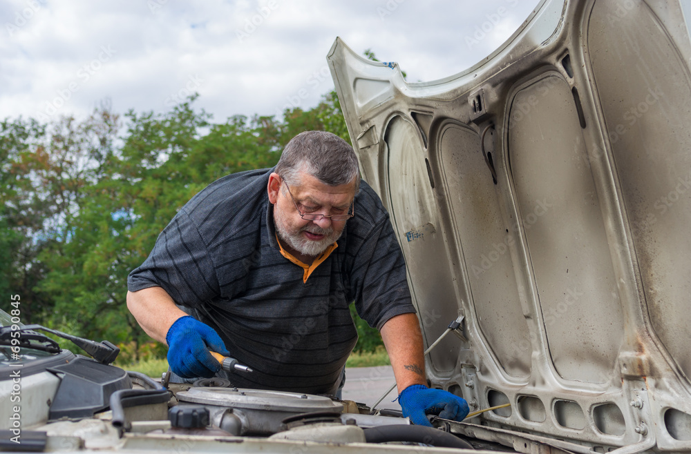 Old man doing car repair on the road Old man doing car repair on the road