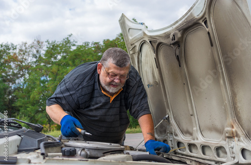 Old man doing car repair on the road