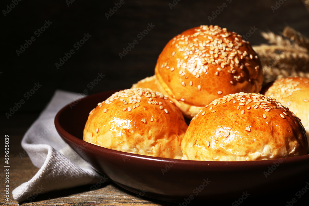 Tasty buns with sesame on plate, on wooden background Tasty buns with sesame on plate, on wooden background