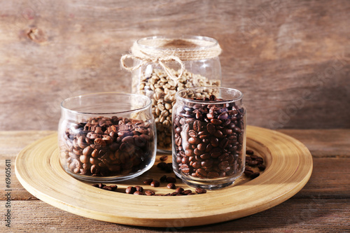 Coffee beans in jars on bamboo plate on wooden background