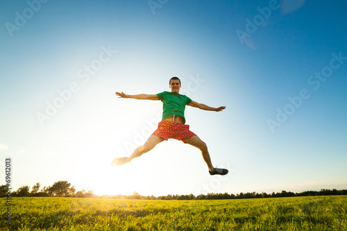 Young man jumping on meadow with dandelions