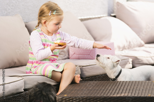 Junges Mädchen sitzt auf Sofa, ißt Donut, streichelt Hund