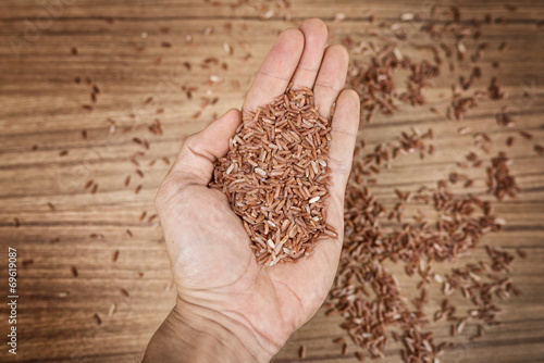 Brown rice in hand on wooden background