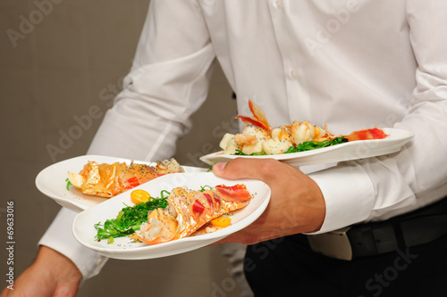 Waiter holds plates with lobsters