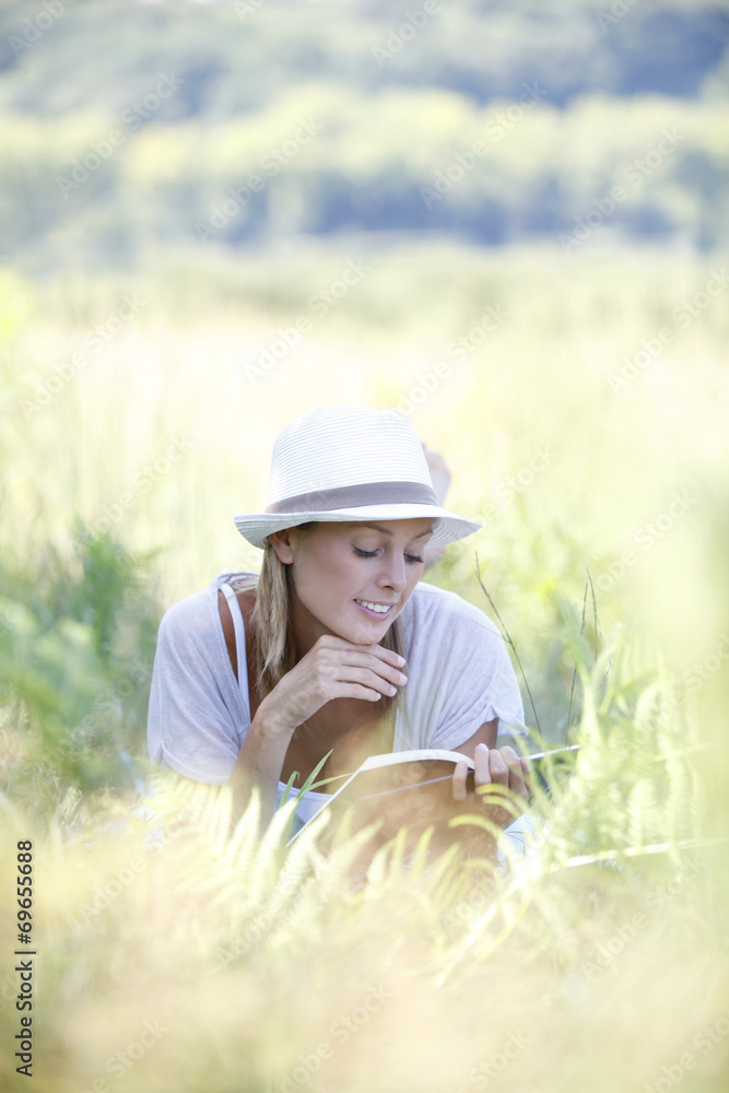 Smiling woman laying in grass and reading book Smiling woman laying in grass and reading book