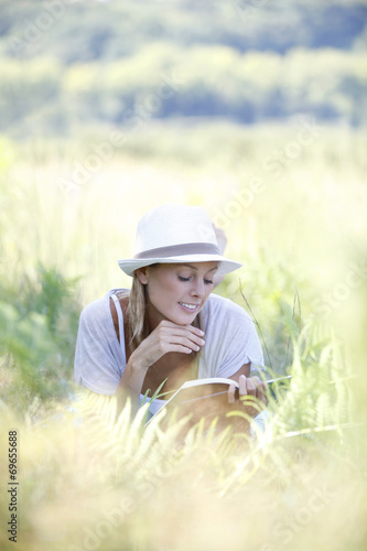 Smiling woman laying in grass and reading book