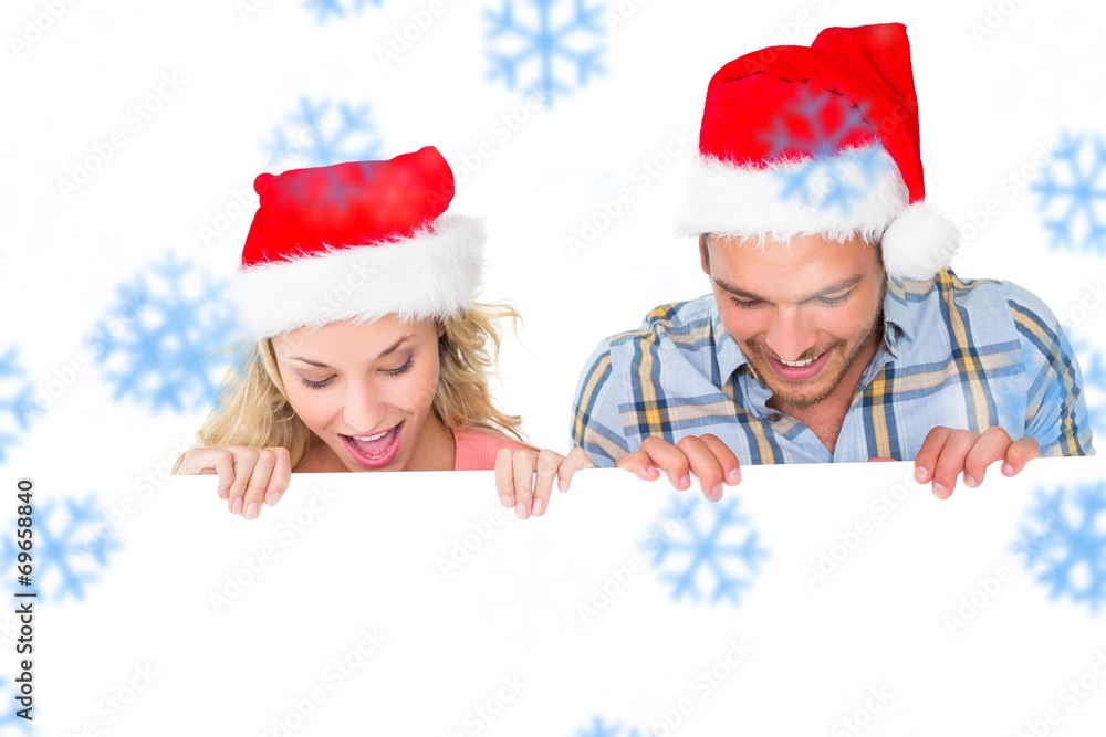 Composite image of festive couple smiling from behind poster Composite image of festive couple smiling from behind poster