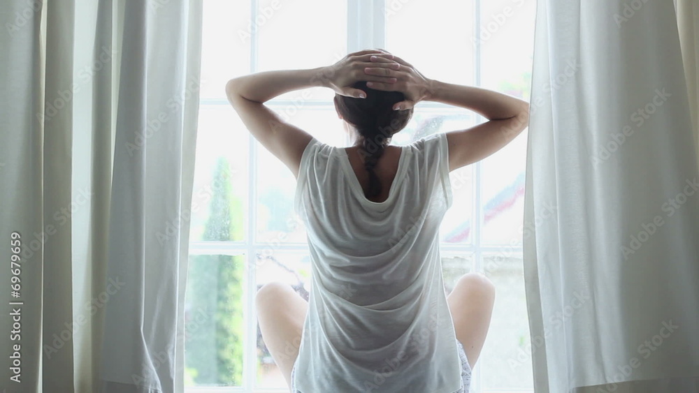 Happy relaxed young woman sits by a window. Rear view Happy relaxed young woman sits by a window. Rear view