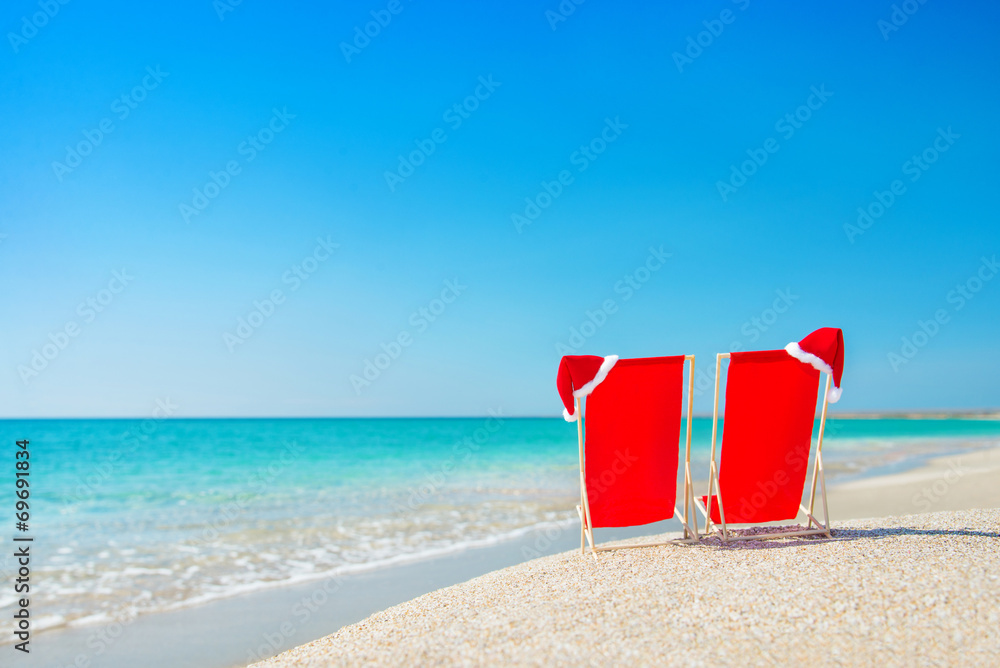 Santa hat on chaise longues at white sand beach against the sea Santa hat on chaise longues at white sand beach against the sea