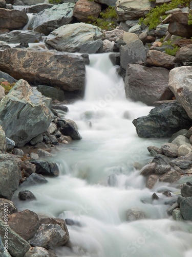 Noisy Alpine stream with with stones. Blurred waves of stream 