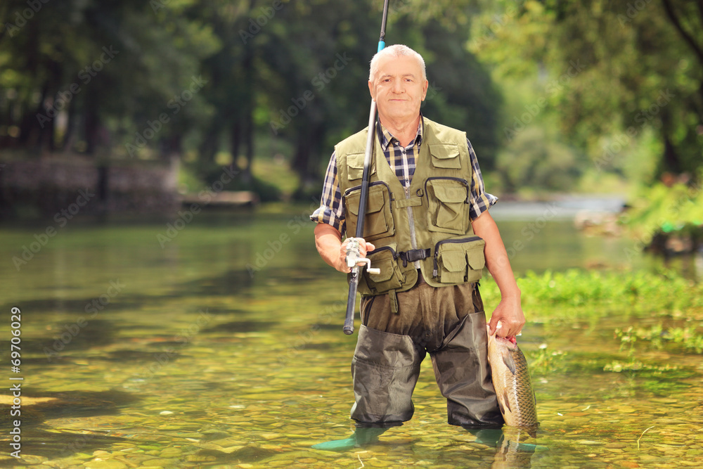 Mature fisherman holding fish in a river Mature fisherman holding fish in a river