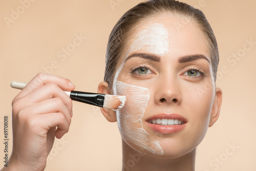 Beautiful girl in spa applying facial cosmetic cream with brush