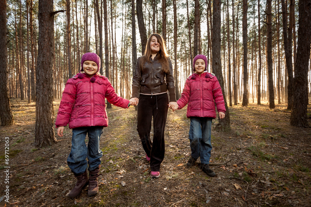mother and two daughters walking at sunny forest