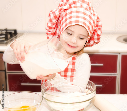 Smiling little girl with chef hat put flour for baking cookies photo